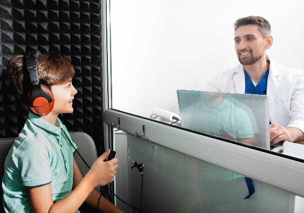 Youth in a sound booth wearing headphones and holding a button