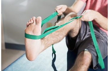 Man sitting doing exercise for foot drop, using strap to pull toes back toward himself
