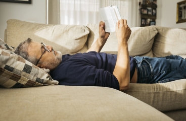 Person lying flat on back on sofa while reading.