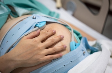 Pregnant person, showing external fetal heart rate monitor sensors placed on belly using belts.