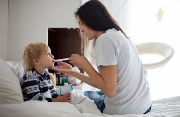 Child sick in bed, showing parent giving child medicine.