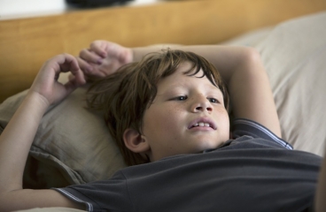 Child lying flat on back on bed.