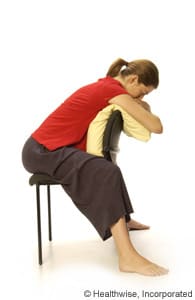 Person sitting backward in a chair and leaning forward over a pillow. Person sitting backward in a chair and leaning forward over a pillow.